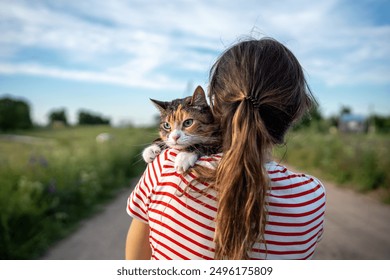 Woman holding quiet tabby cat in arms. Pet looking around, exploring territory with interest, curiosity, feeling cozy, comfortable in hands of female owner. Girl strolling with kitty together. - Powered by Shutterstock