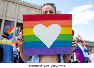 Woman holding rainbow flag heart placard sign, symbol of LGBT love during Pride Parade. Equality march in Krakow, Poland to support and celebrate LGBT+, LGBTQ Gay and lesbian community.
