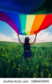 Woman holding the Rainbow Flag on a green meadow outdoors. Happiness, freedom and love concept for same sex couples. 
