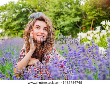 Woman holding a rat in her hands against the background of lavender in the garden. Rat is a symbol of 2020 according to the Eastern calendar.