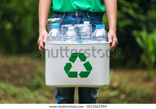 A woman holding a recycle bin with plastic\
bottles in the outdoors