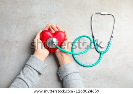 Woman holding red heart and stethoscope on gray background, top view. Cardiology concept