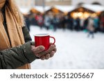 Woman holding red mug with mulled wine or hot drink punch in traditional Christmas market. Enjoyment of advent holiday in city