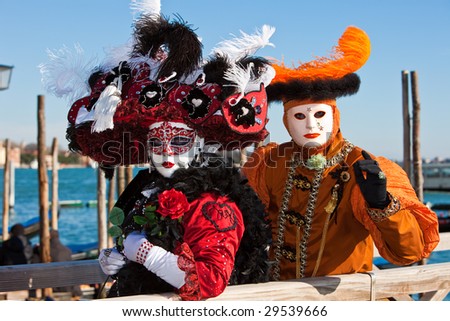 Woman holding a red rose in a black costume with a man in an orange costume at the Venice Carnival