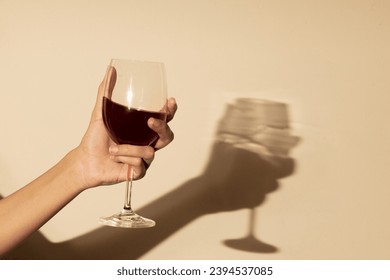 Woman holding a red wine glass on orange background, in direct sunlight