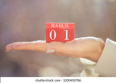 the woman is holding a red wooden calendar. Red wooden cube shape calendar for MARCH 1 with hand 