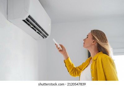 Woman holding remote control aimed at the air conditioner. - Shutterstock ID 2120547839