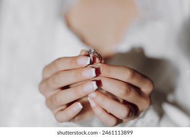 A woman is holding a ring in her hand. The woman is wearing a white dress and has her nails painted. Concept of love and commitment