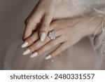 A woman is holding a ring with a large diamond in the center. The ring is white and has a flower design. The woman