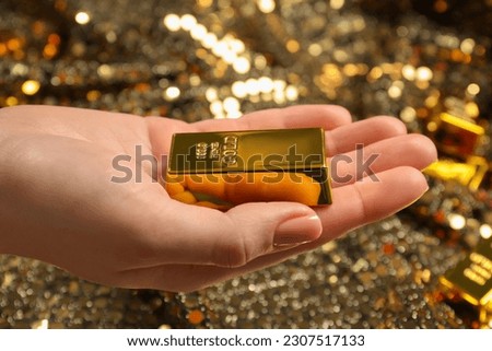 Woman holding shiny gold bar against sequin fabric, closeup