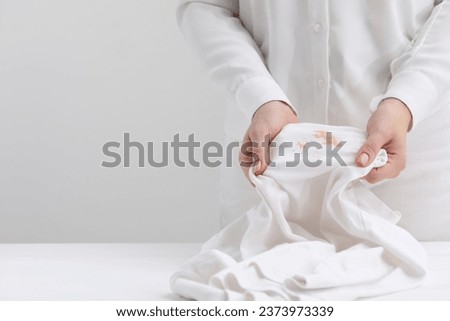 Woman holding shirt with stain at table against light background, closeup. Space for text