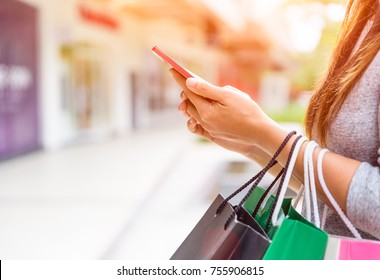 Woman holding shopping bags doing online shopping on her mobile phone in the supermarket. Black Friday sale concpt. Foto Stock