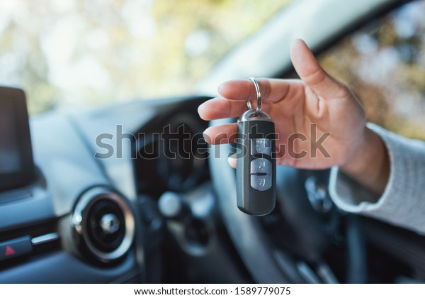 A woman holding and showing car key while sitting in\
the car