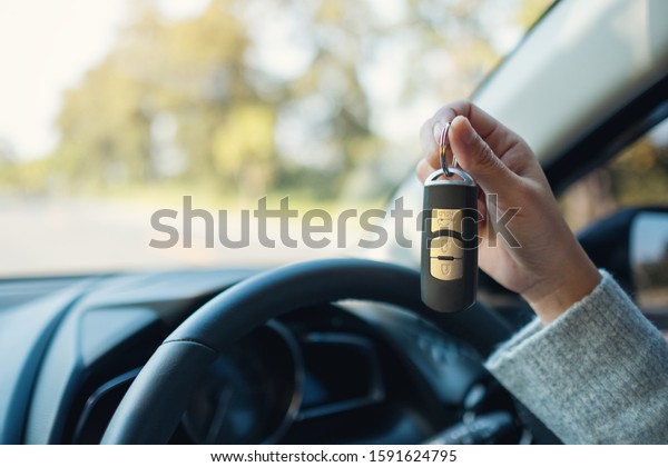 A woman holding and showing car key while sitting in\
the car