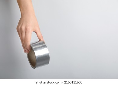 Woman holding silver adhesive tape on light background, closeup. Space for text - Shutterstock ID 2160111603