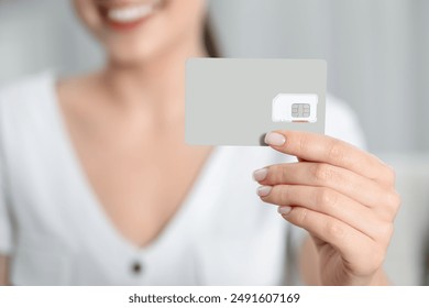 Woman holding SIM card indoors, closeup view - Powered by Shutterstock