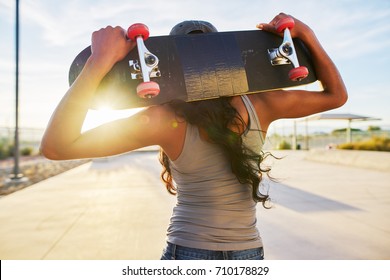 woman holding skate board behind her back looking at sunset shot with lens flare - Powered by Shutterstock