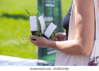 Woman is holding small plants in pots with blank labels at a farmers market, ready to write the names - Powered by Shutterstock