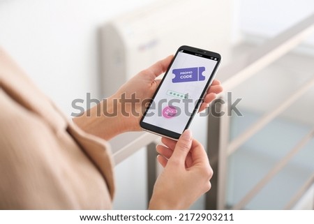 Woman holding smartphone with activated promo code in online shopping app indoors, closeup
