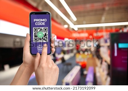 Woman holding smartphone with activated promo code in shopping mall, closeup