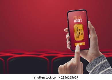Woman holding a smartphone and buying movie tickets online using a mobile app, cinema hall and seats in the background, POV shot