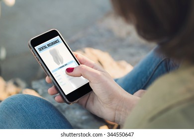 woman holding a smartphone with dental insurance on screen. All screen graphics are made up. - Shutterstock ID 344550647