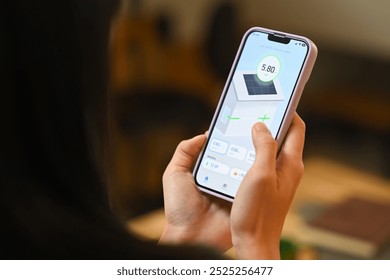 Woman holding a smartphone, displaying an app that monitors solar panel energy usage. Renewable energy systems concept. - Powered by Shutterstock