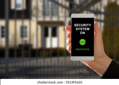 Woman Holding A Smartphone With Home Security System Panel On Blurred House Background

