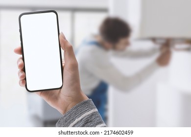 Woman holding a smartphone and plumber fixing a boiler in the background, home repair service concept