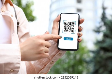 Woman holding smartphone with QR code on screen outdoors, closeup