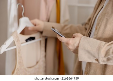 Woman Holding Smartphone And Taking Photo Of Her Old Clothes To Sell Them Online. Selling On Website, E-commerce. Reuse, Second-hand Concept. Conscious Consumer, Sustainable Lifestyle. Close-up View.