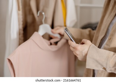 Woman Holding Smartphone And Taking Photo Of Her Old Clothes To Sell Them Online. Selling On Website, E-commerce. Reuse, Second-hand Concept. Conscious Consumer, Sustainable Lifestyle. Close-up View.