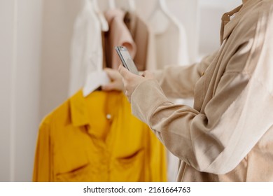 Woman Holding Smartphone And Taking Photo Of Her Old Clothes To Sell Them Online. Selling On Website, E-commerce. Reuse, Second-hand Concept. Conscious Consumer, Sustainable Lifestyle. Close-up View.