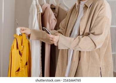 Woman Holding Smartphone And Taking Photo Of Her Old Clothes To Sell Them Online. Selling On Website, E-commerce. Reuse, Second-hand Concept. Conscious Consumer, Sustainable Lifestyle. Close-up View.