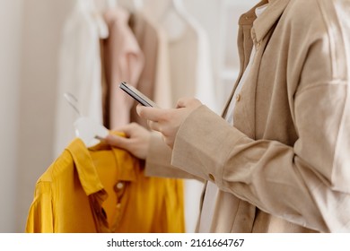 Woman Holding Smartphone And Taking Photo Of Her Old Clothes To Sell Them Online. Selling On Website, E-commerce. Reuse, Second-hand Concept. Conscious Consumer, Sustainable Lifestyle. Close-up View.