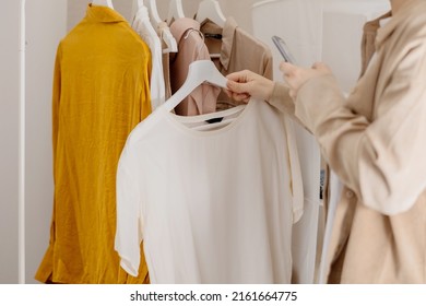 Woman Holding Smartphone And Taking Photo Of Her Old Clothes To Sell Them Online. Selling On Website, E-commerce. Reuse, Second-hand Concept. Conscious Consumer, Sustainable Lifestyle. Close-up View.