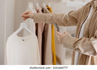 Woman Holding Smartphone And Taking Photo Of Her Old Clothes To Sell Them Online. Selling On Website, E-commerce. Reuse, Second-hand Concept. Conscious Consumer, Sustainable Lifestyle. Close-up View.