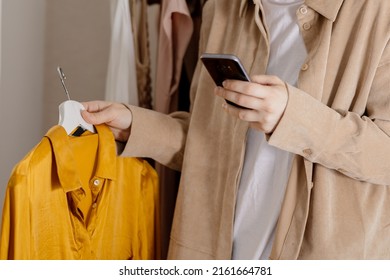 Woman Holding Smartphone And Taking Photo Of Her Old Clothes To Sell Them Online. Selling On Website, E-commerce. Reuse, Second-hand Concept. Conscious Consumer, Sustainable Lifestyle. Close-up View.