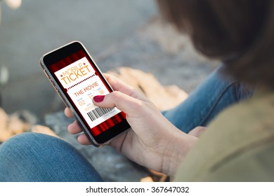 woman holding a smartphone and touching the screen with cinema e-ticket. All screen graphics are made up.