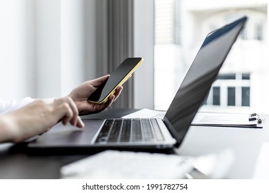 A Woman Holding A Smartphone And Using A Laptop Uses A Smartphone. Chat With Friends Through Instant Messaging To Discuss Business Together And Use Your Laptop To Find Information On The Web.