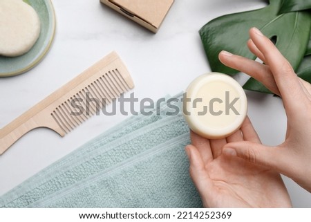 Woman holding solid shampoo bar at marble table, top view. Hair care