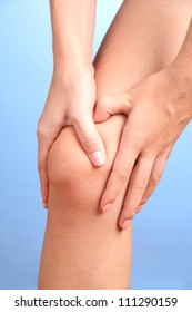 Woman Holding Sore Knee, On Blue Background