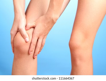 Woman Holding Sore Knee, On Blue Background