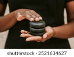 Woman holding spa stones for massage. Black spa staff woman holding relaxing hot stones massage. African American woman holding spa stones for massage. Stones for stone therapy in the hands.