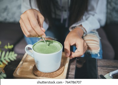 Woman holding spoon and stirring hot green tea matcha latte at cafe. - Powered by Shutterstock