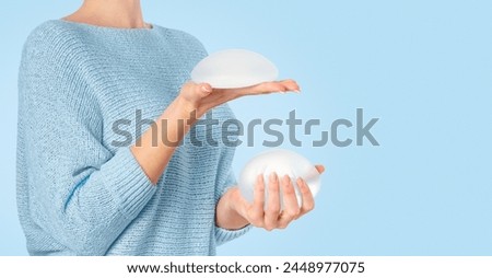 Woman holding and squeezing round implants on blue background. Mammoplasty and plastic surgery.