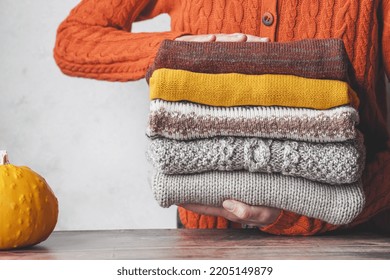 A woman holding a stack autumn warm knitted sweaters. Change of season and wardrobe. autumn slow fashion concept