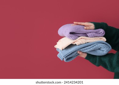 Woman holding stack of different stylish sweaters on burgundy background - Powered by Shutterstock