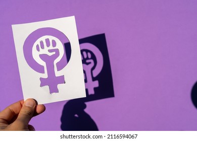 A woman holding the symbol of the fight for feminism on a purple background, clenched fist of a woman at the march protests for women's rights and equality