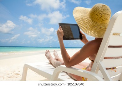 Woman holding tablet computer sitting on the beach in deck chair and taking sun bath - Powered by Shutterstock